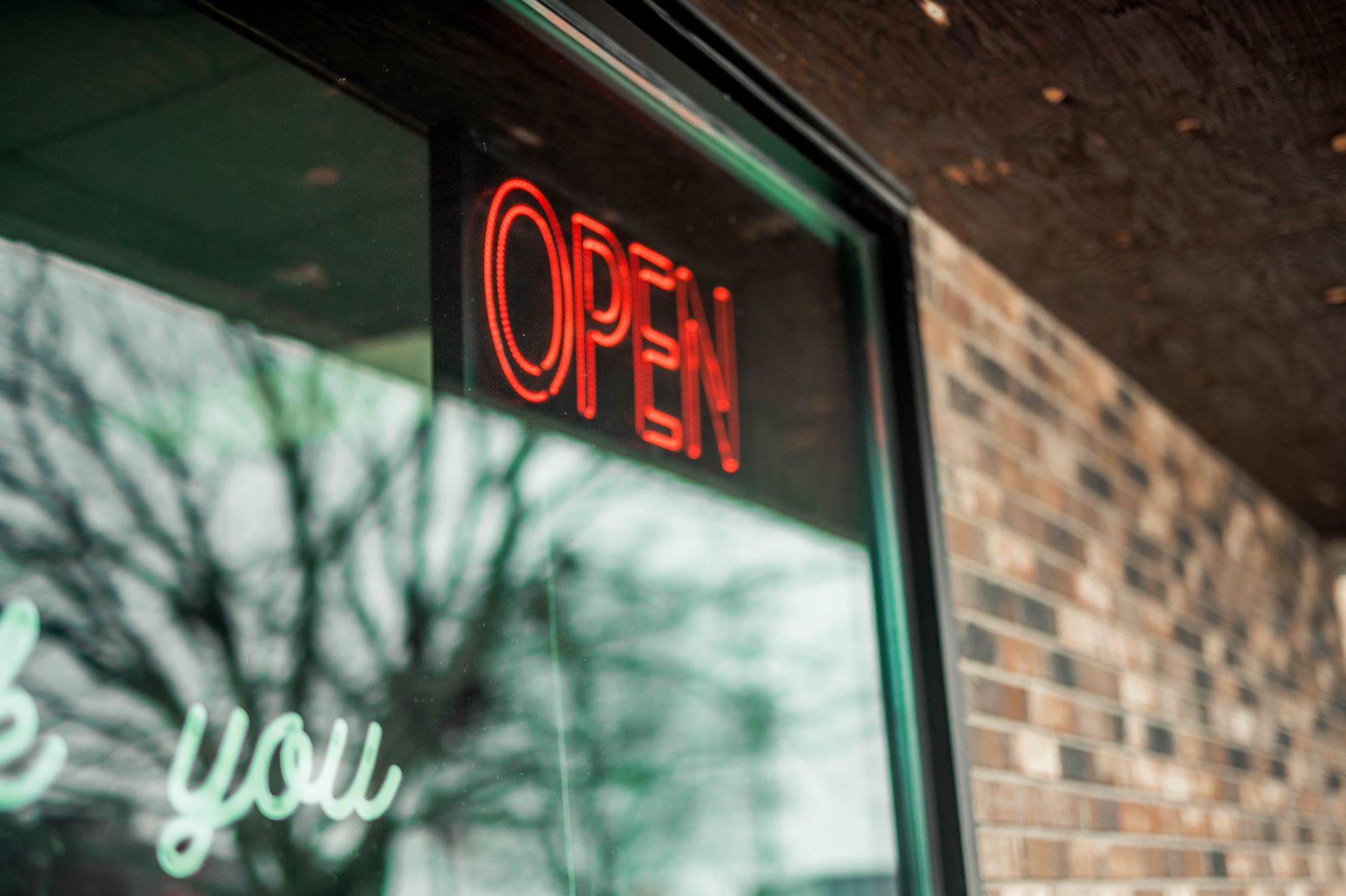 Red neon Open sign glowing in a local business storefront window on a brick building