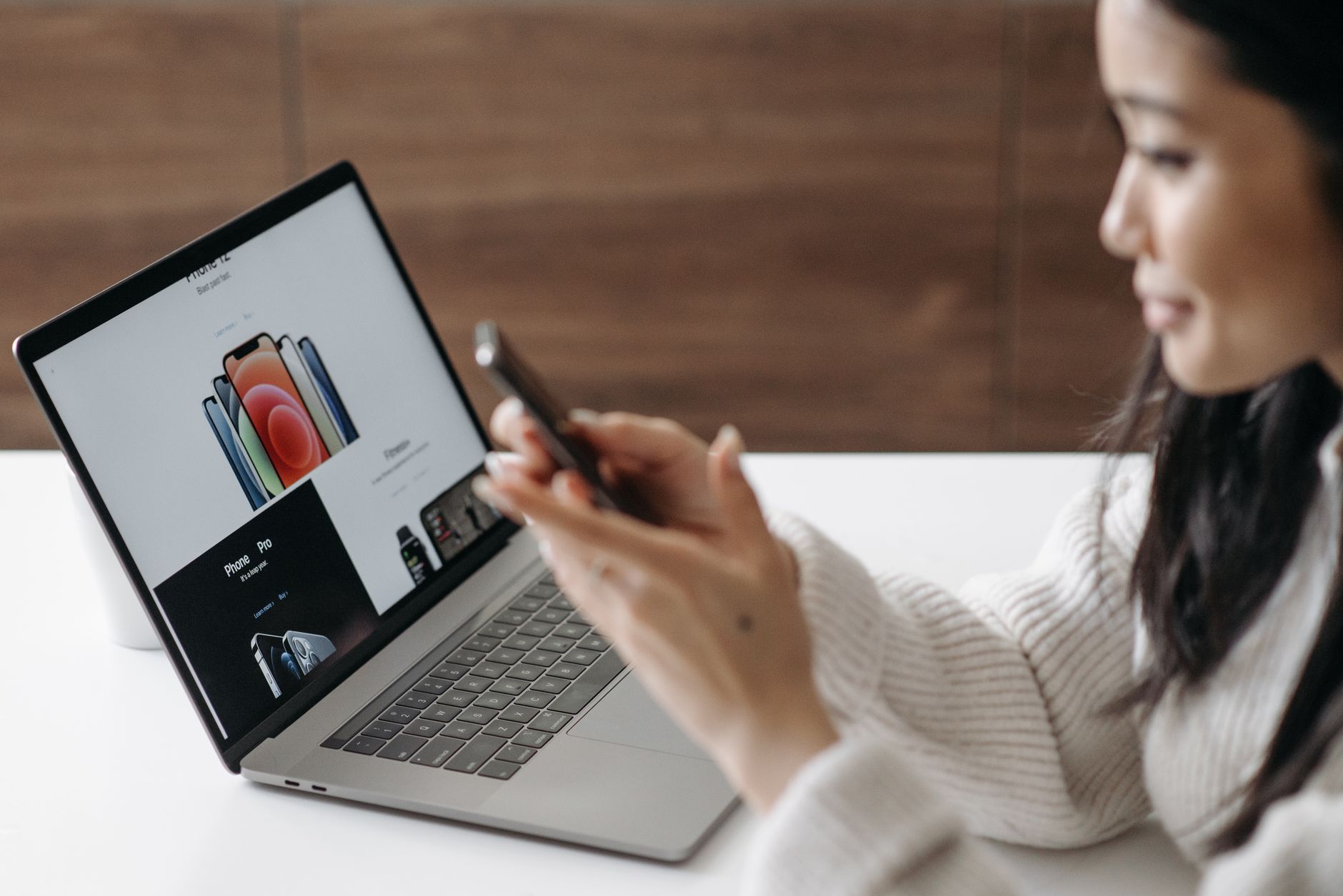 Woman browsing an ecommerce product page on a laptop while holding a smartphone, representing the importance of optimized product pages for SEO