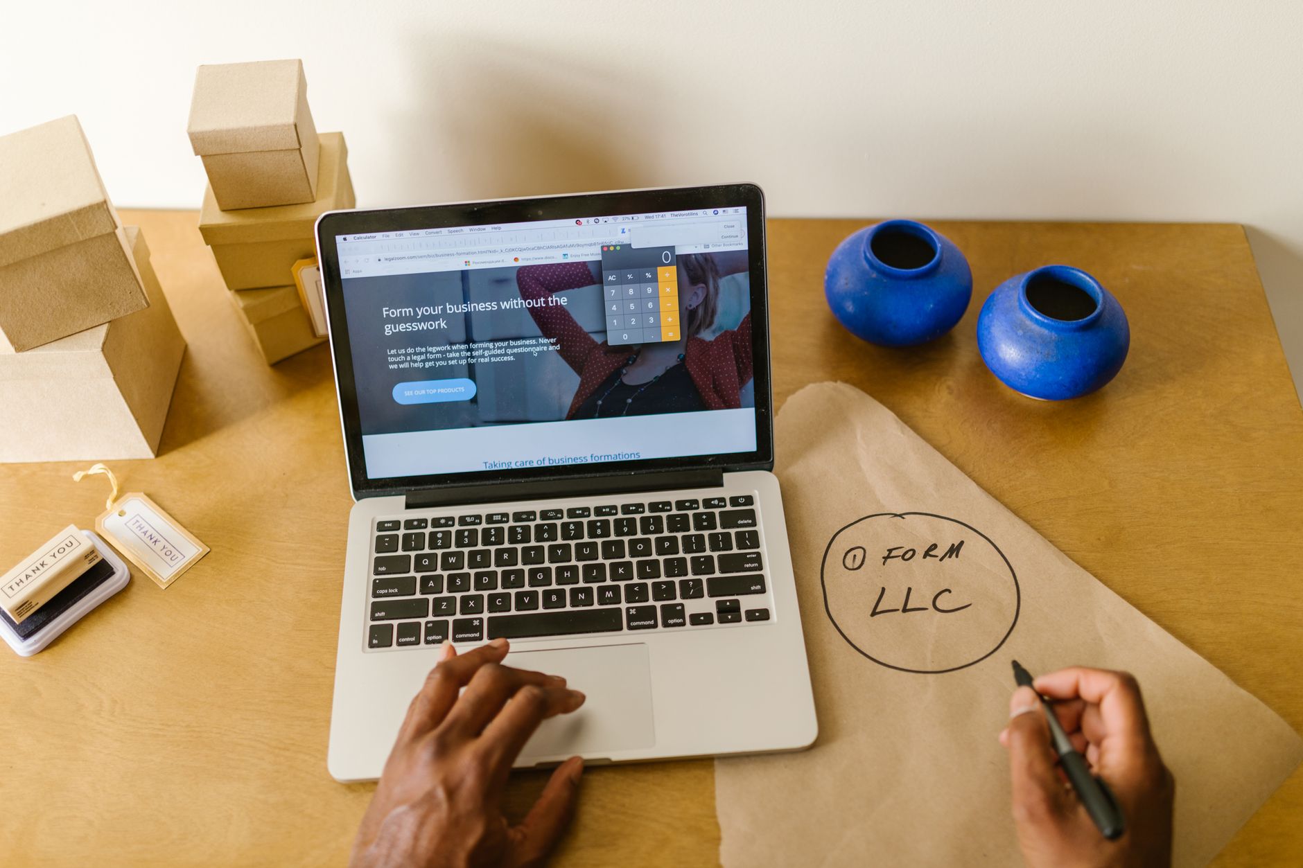 Small business owner working at a desk with a laptop, packaging, and handwritten business notes