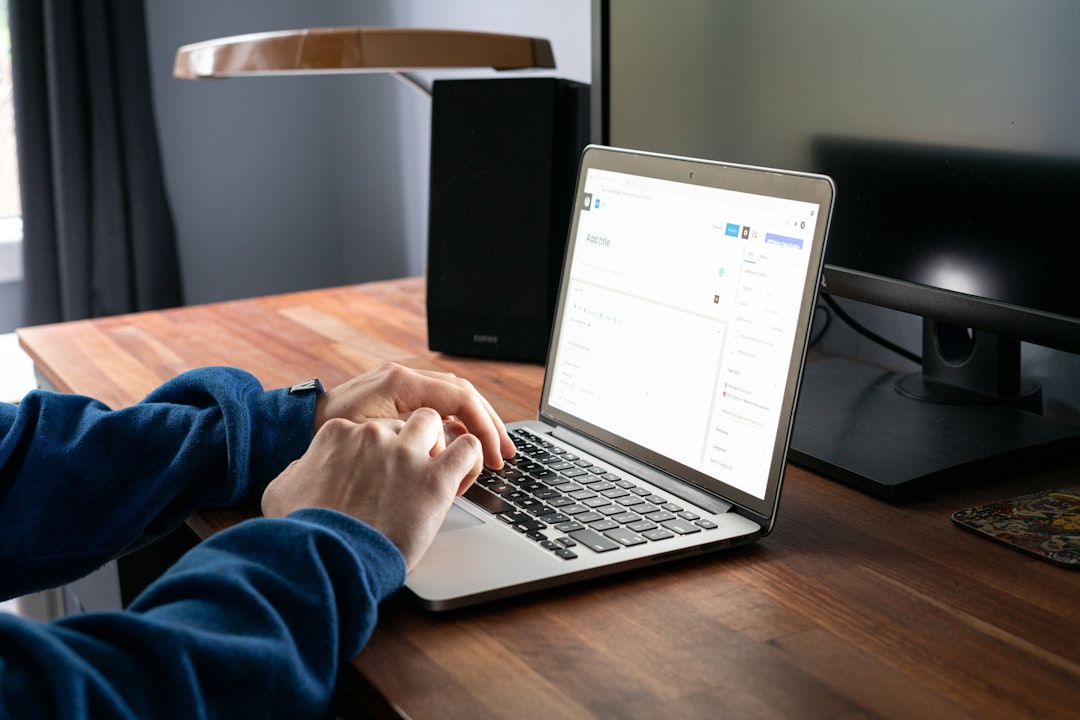Person typing a new WordPress post on a MacBook at a wooden desk