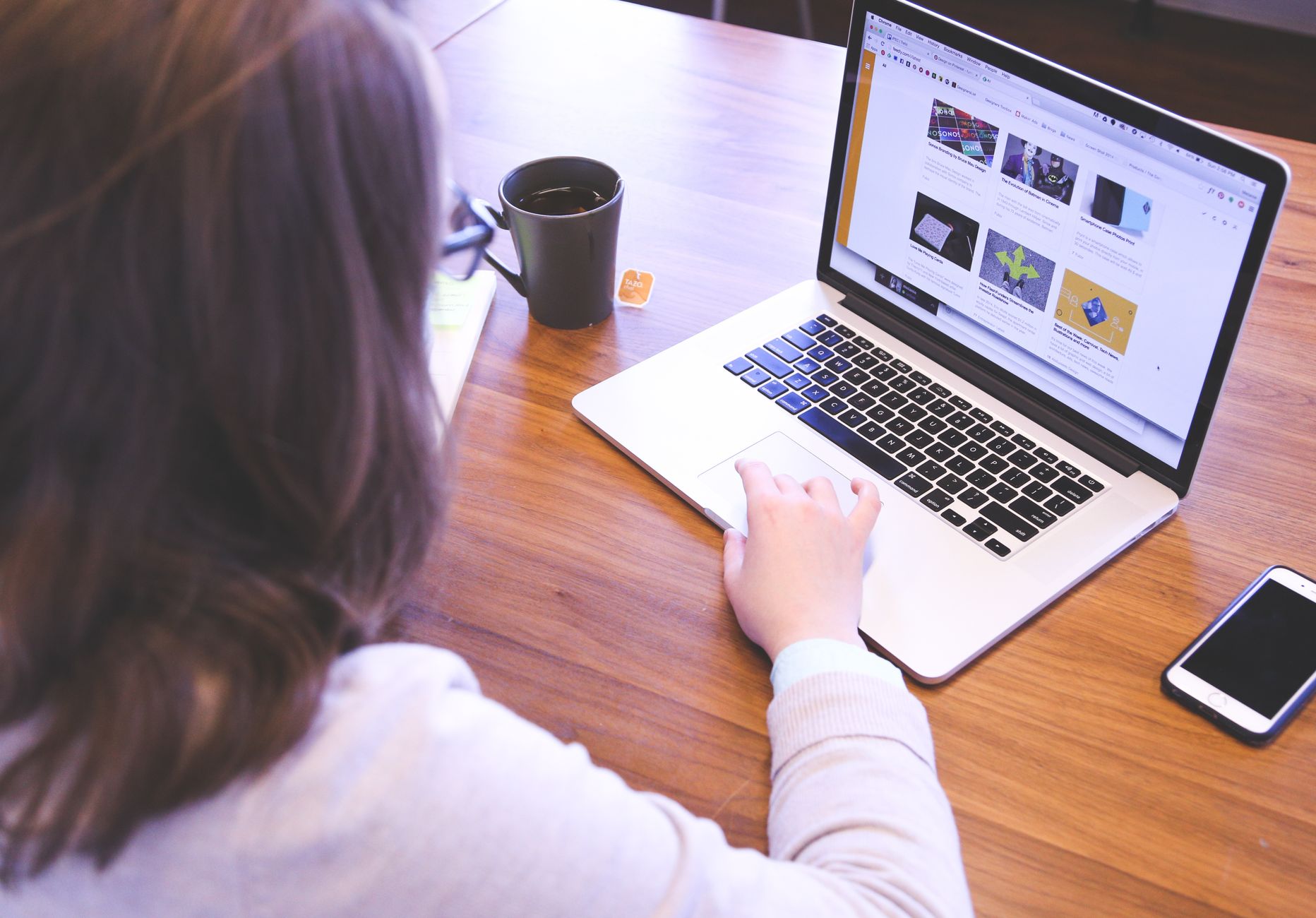 Person browsing and editing website pages on a MacBook at a wooden desk with a smartphone nearby